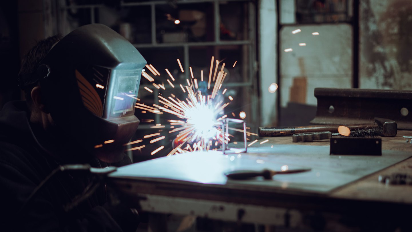 Saldatore con scintille luminose in un'officina buia.